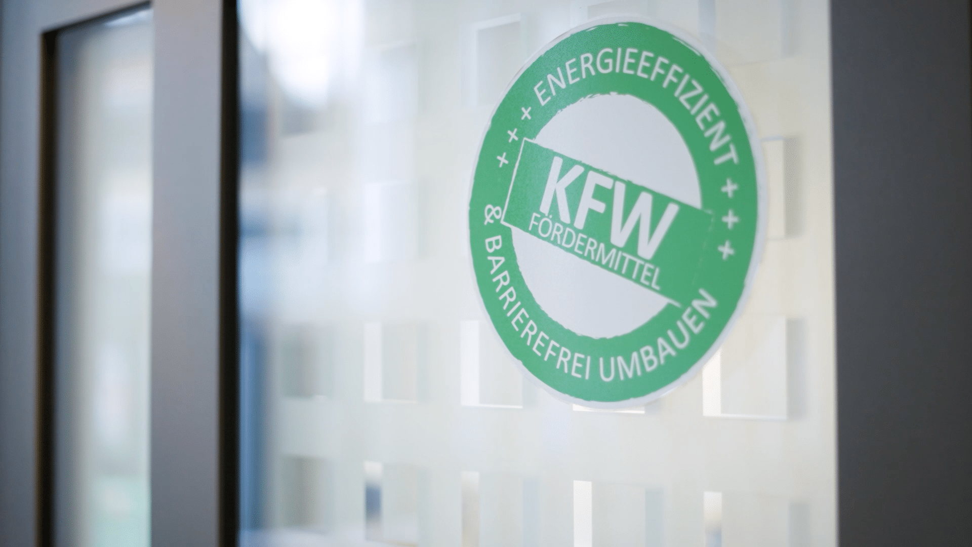 Rundes KFW-Emblem auf einer Glasoberfläche, das energieeffizientes und barrierefreies Umbauen betont.